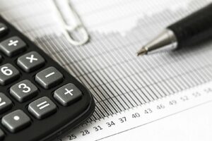 Gros plan d'une calculatrice et d'un stylo sur un graphique à barres, représentant la finance et la comptabilité.