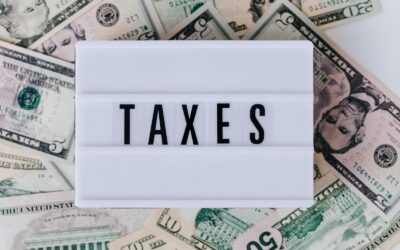 Vue de dessus d'une boîte lumineuse vintage blanche avec l'inscription TAXES placée sur une pile de billets de dollars américains sur une surface blanche