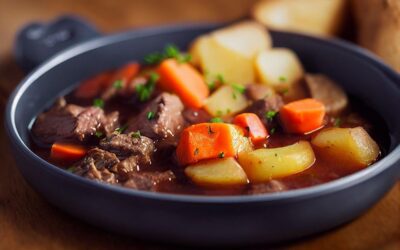 Bol de bouillon contenant viande, carottes, pommes de terre, persil, sur planche