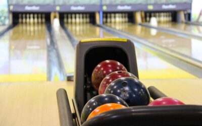 Des balles colorées dans un porte-balles au bowling, voies et quilles visibles